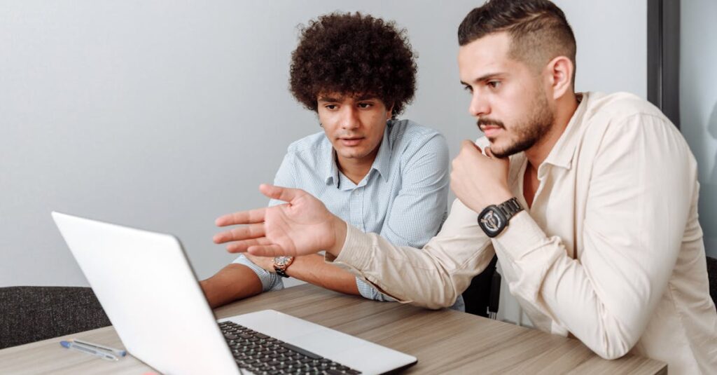 Two young men working together on a laptop in a modern office setting.
